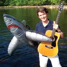 Man with guitar holding a blow up shark