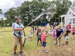 Man with large bubble wand and children chasing bubbles